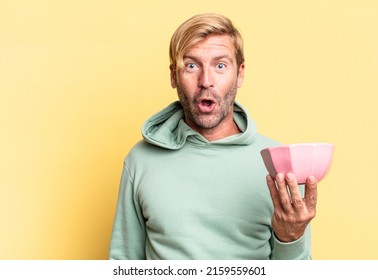 blonde handsome adult man holding an empty pot against yellow wall