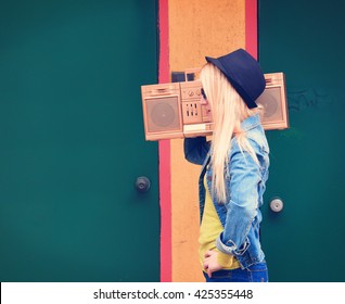 A blonde hipster girl with glasses is listening to a vintage gold boombox radio with a speaker for a music entertainment concept.