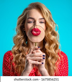 Blonde Holds A Magnifying Glass In Front Of Her Red Lips. Girl With A Big Red Lips Zoomed By Loupe. Smile. Pretty Model Is Flirting.  Young Woman Holds A Magnifying Glass In Front Of Her  Lips.   