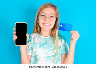 Blonde Kid Girl With Spectacles Wearing Fashion T-shirt  Opened Bank Account, Holding Smartphone And Credit Card, Smiling, Recommend Use Online Shopping Application