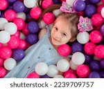 A blonde little girl lying on colorful plastic balls in a large dry children