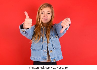 Blonde Little Kid Girl Wearing Denim Jacket Over Red Background  Showing Thumbs Up And Thumbs Down, Difficult Choose Concept