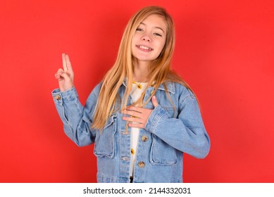 Blonde Little Kid Girl Wearing Denim Jacket Over Red Background  Smiling Swearing With Hand On Chest And Fingers Up, Making A Loyalty Promise Oath.