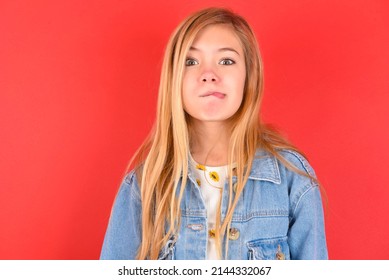 blonde little kid girl wearing denim jacket over red background  making grimace and crazy face, screaming out of control, funny lunatic expressing freedom and wild.