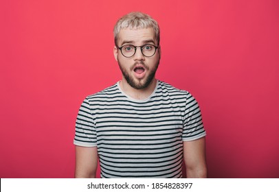 Blonde Mann ist erstaunt über etwas, während man die Kamera durch eine Brille auf einer roten Studiowand anschaut