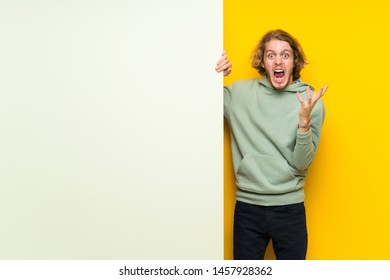 Blonde man holding a big empty placard unhappy and frustrated with something