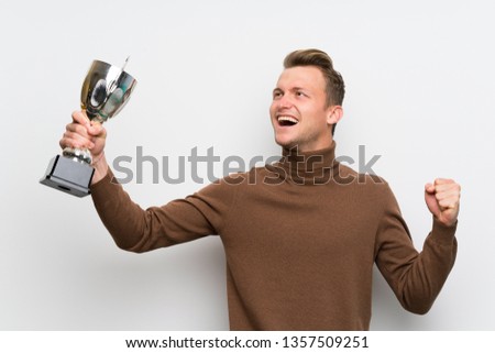 Blonde man over isolated white wall holding a trophy