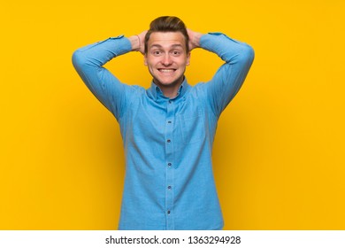 Blonde man over isolated yellow wall frustrated and takes hands on head - Shutterstock ID 1363294928