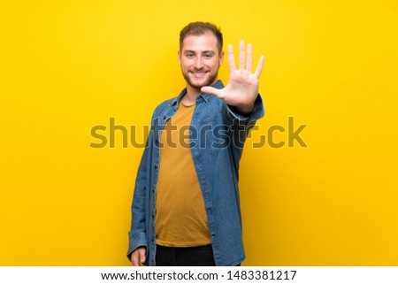 Blonde man over isolated yellow wall counting five with fingers
