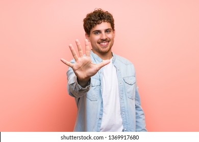 Blonde Man Over Pink Wall Counting Five With Fingers