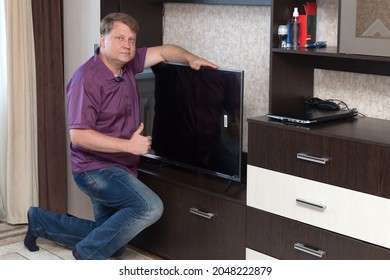 Blonde Man In A Purple Shirt Installs A New LCD TV On The Bedside Table.
