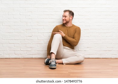 Blonde man sitting on the floor extending hands to the side for inviting to come