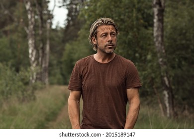 Blonde Man With A Stubble Beard In A Brown T-shirt On A Forest Path In The Summer. Front View.