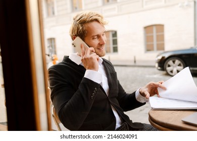 Blonde Man Talking On Cellphone While Working With Papers In Cafe Outdoors