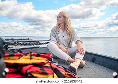 A blonde mature woman in white clothes sitting on a boat and looking dreamy