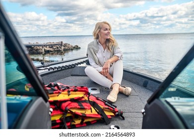 A blonde mature woman in white clothes sitting on a boat and looking dreamy