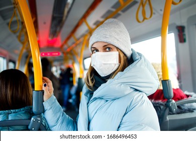 Blonde In Medical Mask Standing In Bus Lounge Next To Yellow Handrails In Afternoon.