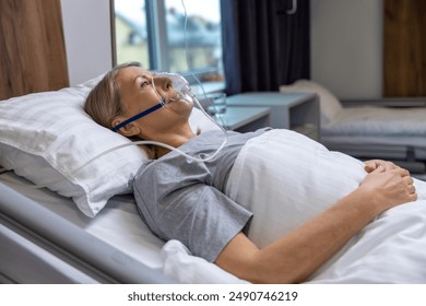 Blonde mid aged woman lying in bed in hospital with an oxygen mask on her face - Powered by Shutterstock