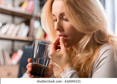 Blonde Middle Aged Woman Holding Glass With Water And Taking Pill 