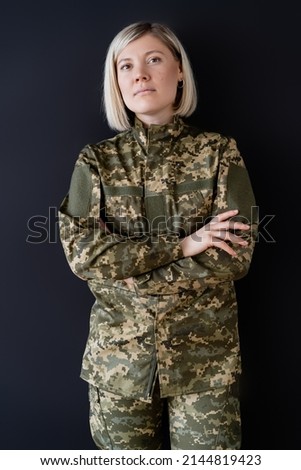 blonde military woman standing with crossed arms and looking at camera isolated on black