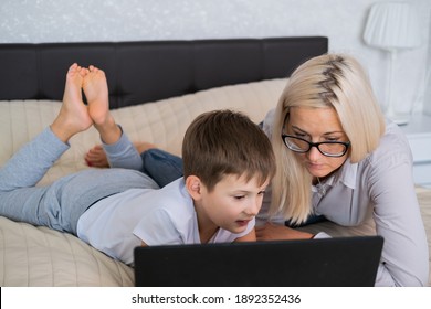 Blonde Mom With Glasses And Teen Son Look At The Laptop Screen While Lying On Couch. Education At Home In Quarantine. Lockdown