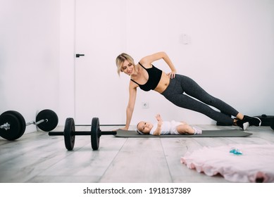 A Blonde Mother Is Doing Fitness With Her Little Baby On The Floor In The Room. Postpartum Health And Recovery Concept. Place For Text.