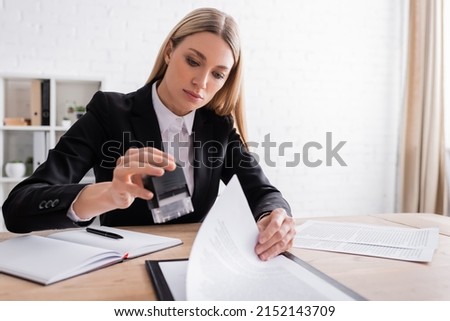 blonde notary holding stamper while working with documents in office