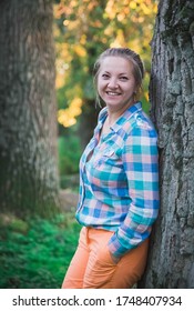blonde in orange trousers and a plaid shirt smiling in the forest  - Shutterstock ID 1748407934