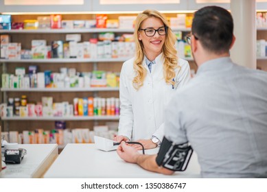 Blonde Pharmacist Measuring Blood Pressure To Young Male Patient.