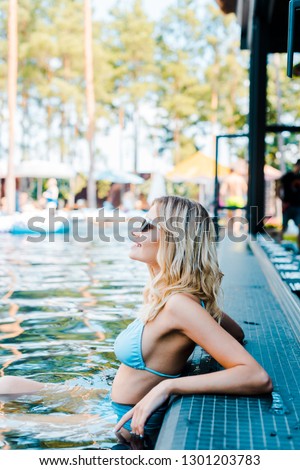 blonde pin up girl in blue swimsuit resting in swimming pool