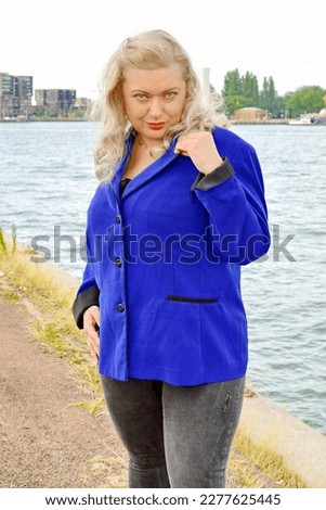 Blonde plus size model wearing blue jacket nature water background travelling travel posing in nature blog glamout fashion article