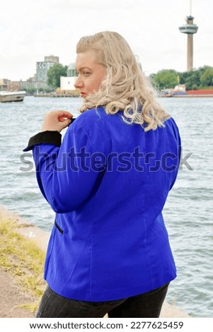 Blonde plus size model wearing blue jacket nature water background travelling travel posing in nature blog glamout fashion article