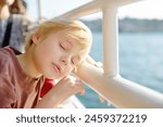 Blonde preteen boy is traveling by boat or ferry on the sea. Family vacations on ocean or sea. Summer leisure for families with kids. Child overheated on a hot sunny day. Bored child on holiday trip
