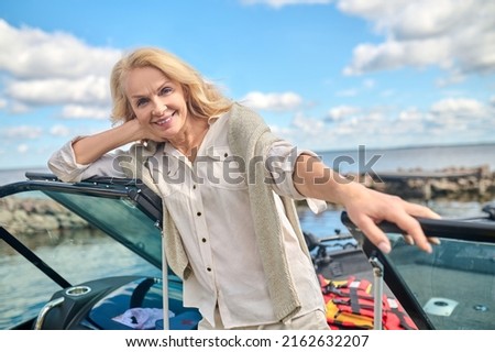 A blonde pretty woman standing on a boat deck and smiling