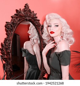 A blonde with retro hair and make-up stands in the mirror. Hollywood Wave. Old Hollywood look. Portrait of a beautiful girl in a glamorous outfit