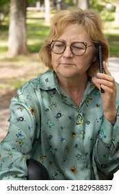 Blonde Senior Sitting Woman In Her 60s, With A Green Blouse With Insects, Having A Difficult Conversation With Her Mobile Phone	
