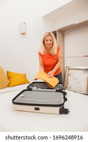 Blonde Senior Woman Packing Her Clothes Into A Suitcase. Travel And Vacation Concept.
