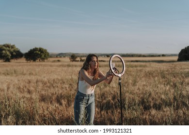 A Blonde Spanish Girl Setting Her Phone Up For A Selfie On A Ring Light In A Sunny Wheat Field