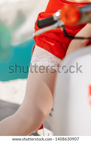 blonde in the style of the 60s in round glasses, white scarf, black top, long red skirt, white stockings on a sandy beach with blue water on a moped under the sun, summer with a cocktail