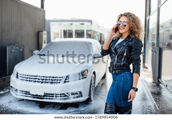 Blonde and sucessful business woman speak by\
phone near her car on wash service\
car.