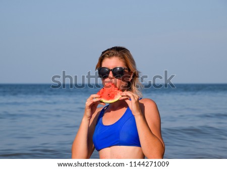 A blonde in sunglasses eats a watermelon by the sea. A juicy watermelon in the hands of a woman.