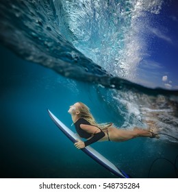 Blonde surfer in bikini with surf board dive under ocean wave lip. Underwater sport activity with fun. Family lifestyle,water sport lessons and beach swimming activity on summer vacation with children