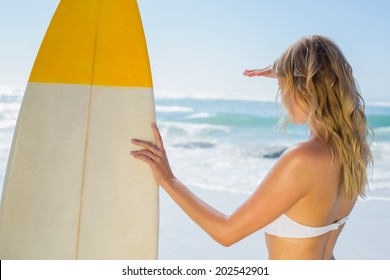 Blonde surfer in white bikini holding her board on the beach on a sunny day - Powered by Shutterstock