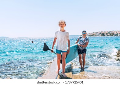 Blonde teenage son with father surfers smiling and carrying the stand-up paddleboard with a paddle on the bright sunny day noon. Active family summer vacation time near the sea concept image. - Powered by Shutterstock