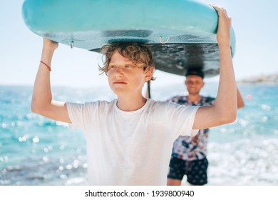 Blonde juenage Sohn mit Vater Surfer lächeln mit dem Stand-up Paddleboard mit einem Paddel am hellen sonnigen Tag Mittag. Aktive Sommerferien für Familien in der Nähe des Meereskonzepts.