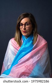 Blonde Transgender Woman With Glasses And LGTB Trans Flag Cape Looking At Camera In A Vertical Portrait Photo