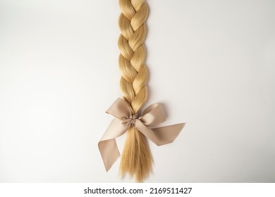 A Blonde Tress With A Beige Bow Lying On A White Background