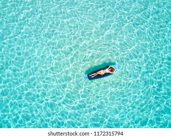 Blonde vacations woman in bikini takes a sunbath on a surfboard over the tropical, turquoise waters of the Maldives