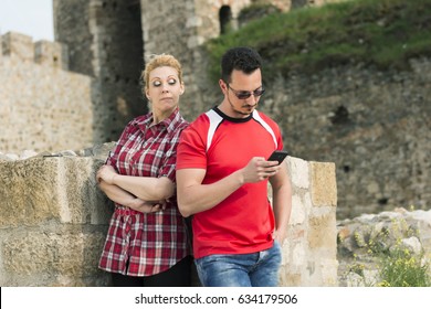 Blonde, Very Tall Girl Peeking Over Her Boyfriend's Shoulder At His Mobile Phone, Outdoor Shot