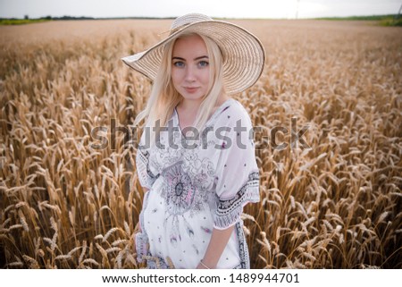 A blonde in a wheat field walks in a straw hat
